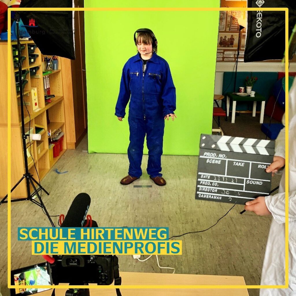 Die Medienprofis.
Ein Schüler in blauem Arbeitsanzug und mit Headset auf steht vor einem Greenscreen. Im Vordergrund ist eine Kamera aufgebaut. Am Rand wird eine Filmklappe ins Bild gehalten.